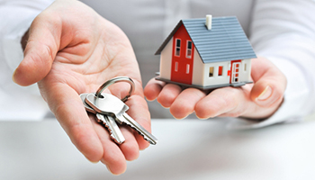 Person holding house key and key to a house